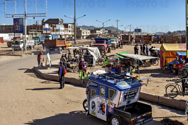 Bustling street scene with tuk-tuk, market stalls and people under bright blue skies, people on the streets of Puno in Peru