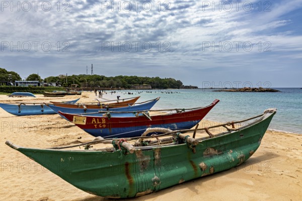 Beach with colorful fishing boats in the sand against a cloudy sky and calm sea, Traditional boats on Trincomalee beach in Sri Lanka