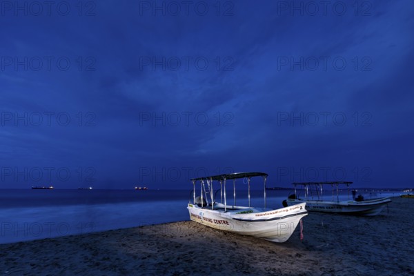 Night landscape with illuminated boat on beach, calm sea and dark sky, traditional boats on Trincomalee beach in Sri Lanka