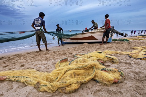 Fishermen on the beach catch up with nets, the sea is calm and the sky is cloudy, Traditional fishermen on Trincomalee beach in Sri Lanka