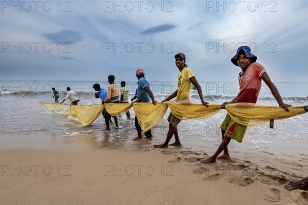 Group of people on the beach leading a fishing net into the water, collective action, traditional fishermen on Trincomalee beach in Sri Lanka