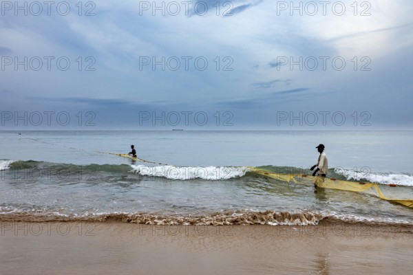 Two fishermen in the sea pull a net across the waves, calm coastal atmosphere, traditional fishermen on Trincomalee beach in Sri Lanka