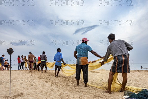 Group of people pulling out a fishing net on the beach, collaborative work at the sea, traditional fishermen on Trincomalee beach in Sri Lanka