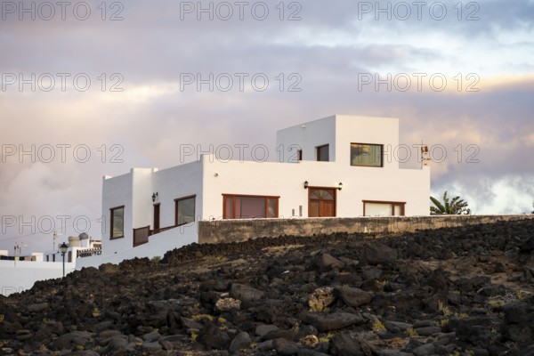 Black coast of volcanic rocks behind typical white houses of the village of La Santa, at sunset, Lanzarote, Canary Islands, Spain