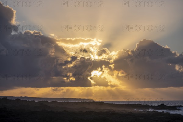 Dramatic cloudy sky with sunbeams at sunset, seaside coast with volcanic rocks, La Santa, Lanzarote, Canary Islands, Spain
