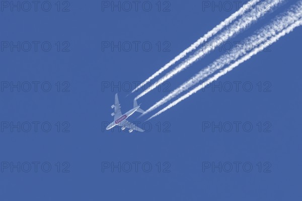 Airbus A380 jet passenger aircraft of Emirates airlines flying in a blue sky with contrails or vapour trails behind, England, United Kingdom