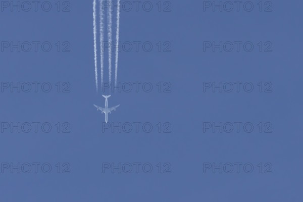 Jet passenger aircraft flying in a blue sky with contrails or vapour trails behind, England, United Kingdom