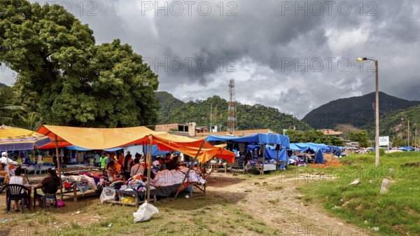 Open-air market with various stalls under orange and blue covers in front of mountains, The market of Rurrenabaque in the Amazon jungle rainforest in Bolivia