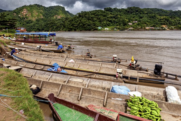 Wooden boats with bananas and motors in front of a mountainous landscape, longboat on a river near Rurrenabaque in the Amazon jungle in Bolivia
