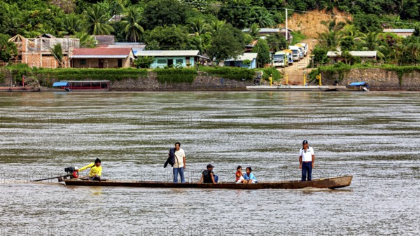 A boat with people passes by a tropical village surrounded by lush nature, people on boats near Rurrenabaque in the Amazon jungle in Bolivia