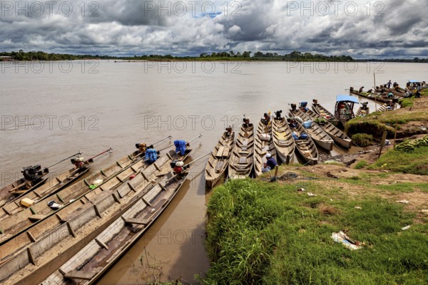 Wooden boats lie on the riverbank under a cloudy sky surrounded by lush greenery, longboat on a river near Rurrenabaque in the Amazon jungle in Bolivia