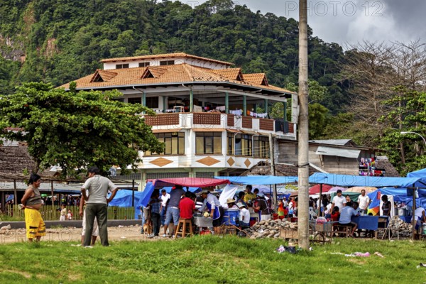 Large house in the background of a busy market square with people and mountains in the distance, The Rurrenabaque market in the Amazon jungle rainforest in Bolivia