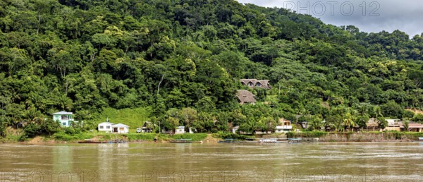 A forest next to a river with houses scattered along the shore under a cloudy sky, the city of Rurrenabaque in the Amazon jungle rainforest in Bolivia
