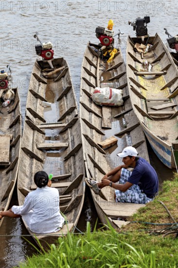 People sit in wooden barges with motors on the banks of a river, longboat on a river near Rurrenabaque in the Amazon jungle in Bolivia