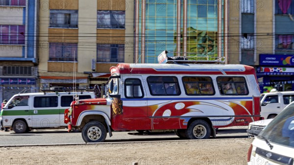 A red and white bus travels through a busy street surrounded by multi-colored buildings, traffic in the city of La Paz in Bolivia