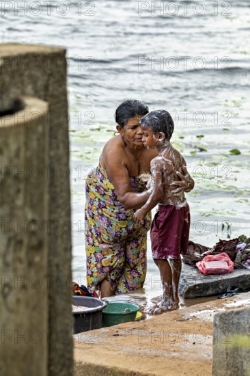 A woman washes a child at the river, both laugh and wear colorful clothes, a woman washes at a lake near Sigiriya in Sri Lanka