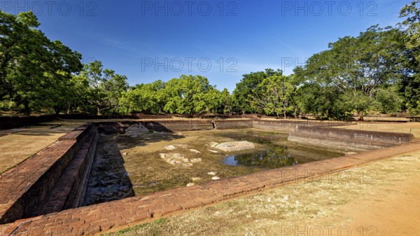An empty brick water pool in a historic setting with green trees, the temples, dagobas, and pagodas at Lion Rock near Sigiriya in Sri Lanka