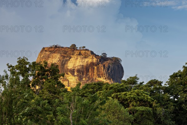 Massive rock juts out of the green landscape under a blue sky, The Lion Rock near Sigiriya in Sri Lanka
