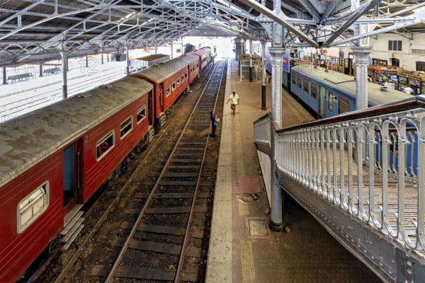 Station with red trains under a metal roof, people on the platform, The station and platform with trains from Colombo in Sri Lanka