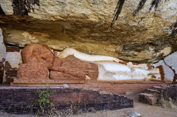 Ancient sandstone sculpture of a Buddha reclining under a rocky outcrop, tranquil setting, The sleeping Buddha at Pidurangala Rock near Sigiriya in Sri Lanka