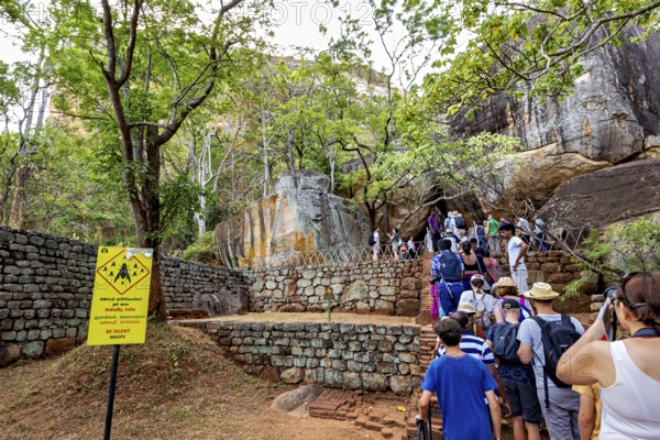 Group of people on a hiking trail next to rocks and trees, tourist environment, tourists at the temples and rocks of Lion Rock near Sigiriya in Sri Lanka