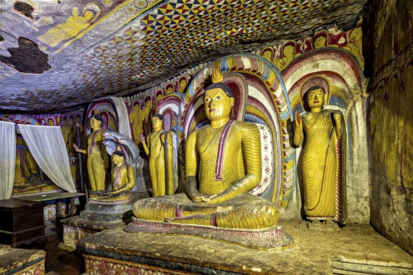 Meditative Buddha statues in a colorful cave with spiritual paintings on the walls, The cave temples of Dambulla in Sri Lanka