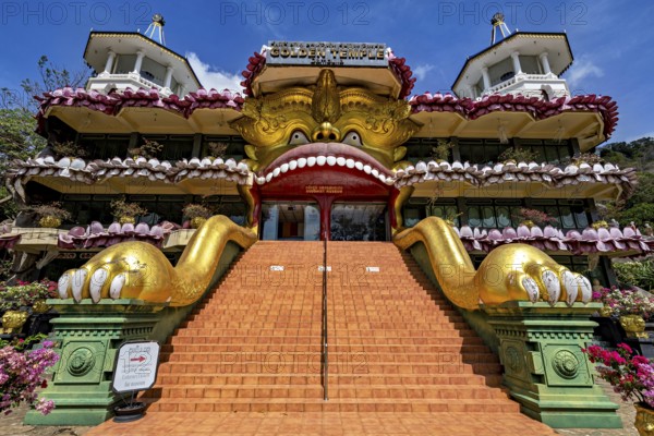 Entrance to a temple with a large golden sculpture and stone stairs decorated with ornaments, The cave temples of Dambulla in Sri Lanka