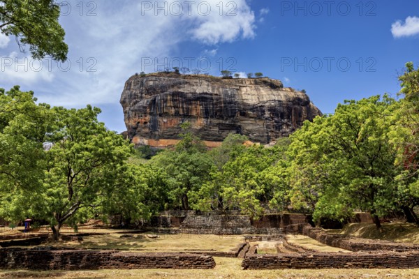 Historic ruins and lush greenery in front of an impressive rock under a blue sky, The Lion Rock near Sigiriya in Sri Lanka