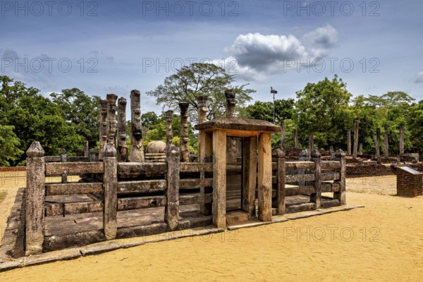 Wooden gate flanked by stone pillars on a sandy floor under a cloudy sky, The temples of Polonnaruwa in Sri Lanka