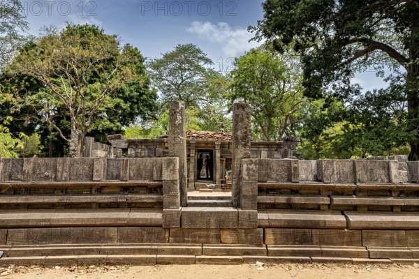 Stone gate marking the entrance to an ancient structure under a clear sky, surrounded by trees, The temples of Polonnaruwa in Sri Lanka