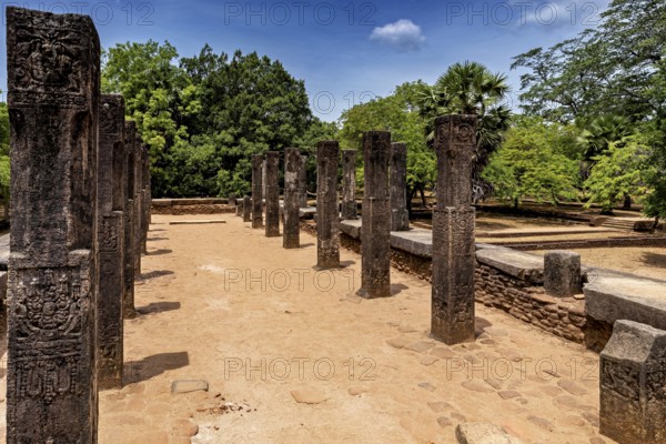 Row of open-air stone pillars on a sunny brick path with trees, The temples of Polonnaruwa in Sri Lanka