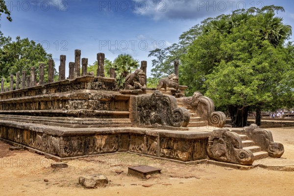 Stone wall with engraved sculptures and stairs surrounded by tall trees, The temples of Polonnaruwa in Sri Lanka