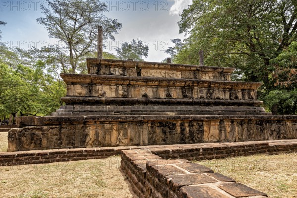 Engraved stone tablet with historical relics under a cloudy sky surrounded by trees, The temples of Polonnaruwa in Sri Lanka