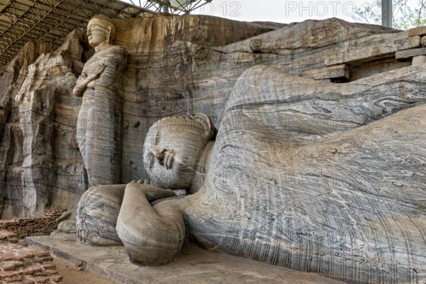 Close-up of the artistic detail of a large reclining Buddha statue next to a standing figure carved out of rocks, The Buddhas at Polonnaruwa in Sri Lanka