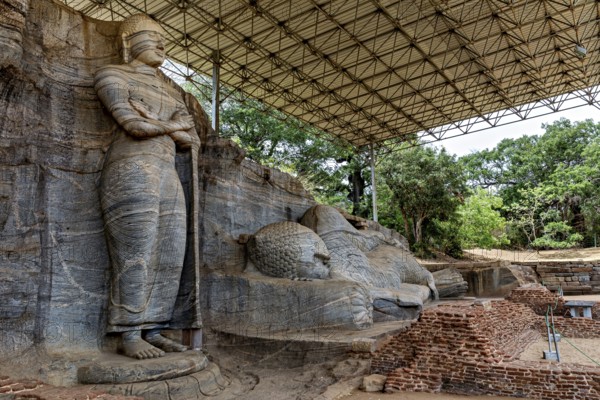 Monumental rock statue with standing and resting figure under a canopy surrounded by nature and brick walls, The Buddhas near Polonnaruwa in Sri Lanka