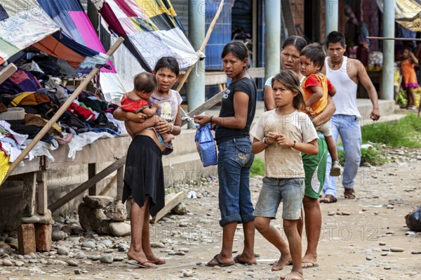 Group of people, including woman and children, stand at a market with colorful stalls, poverty in the streets of Rurrenabaque in the Amazon jungle in Bolivia