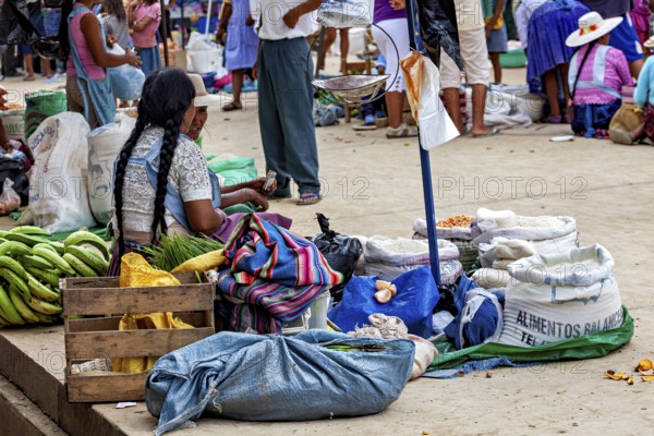 A woman sits in a market surrounded by sacks and bananas and observes the surrounding area, The Rurrenabaque market in Bolivia