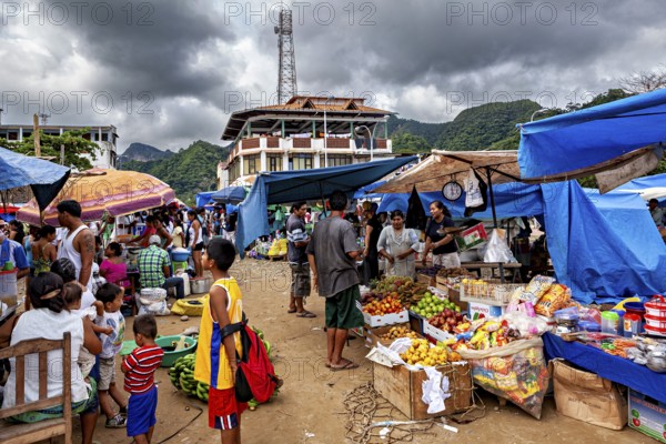 A bustling market with fruit and stalls under ominous clouds and mountain scenery, The Rurrenabaque market in Bolivia