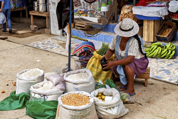 Woman wearing a hat sitting at the market and opening a bag of grain, The Rurrenabaque market in Bolivia