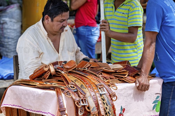 A man sells leather belts at a market stall surrounded by customers, The Rurrenabaque market in Bolivia