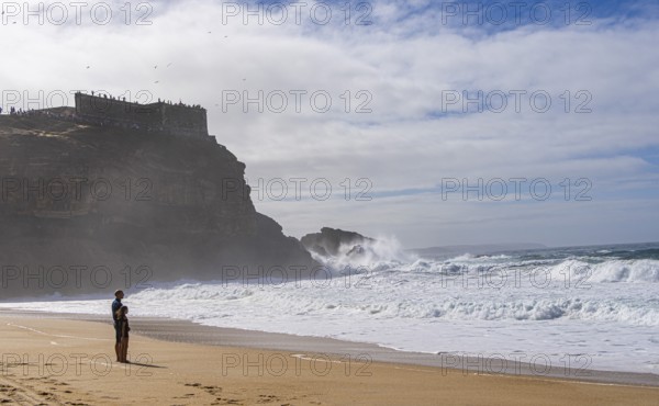 Tourists watch the waves of the Atlantic on the rocky plateau of Sito, also known as Forte São Miguel, a surfing paradise with monster waves in the months of November to February, Nazaré, Portugal