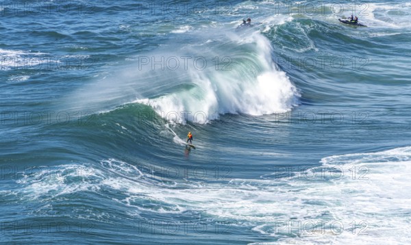 Surfers with their jet ski pilots in the Atlantic waves below Farol de Nazaré, Forte São Miguel, known as a surfer hot spot with monster waves between November and February of each year, Nazaré, Portugal