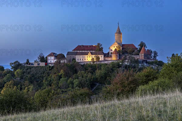 An illuminated castle on a hill at dusk, surrounded by shady trees, The Leuchtenburg near Kahla im Saale Holzlandkreis in Thuringia