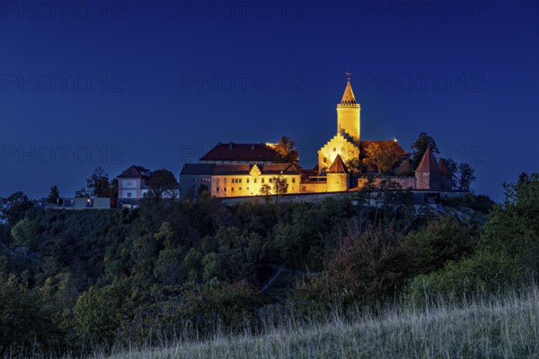 A castle at dusk, illuminated and picturesquely situated on a hill, in contrast to a clear blue sky, The Leuchtenburg near Kahla in the Saale Holzlandkreis district in Thuringia