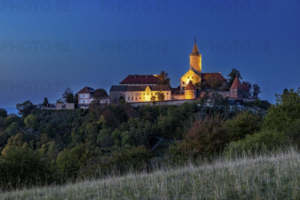 A castle on a wooded hill, illuminated at dusk with dark skies, The Leuchtenburg near Kahla im Saale Holzlandkreis in Thuringia