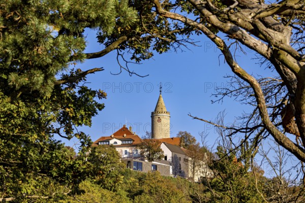 A castle with a tower, framed by trees and branches, in front of a clear autumn sky, The Leuchtenburg near Kahla im Saale Holzlandkreis in Thuringia