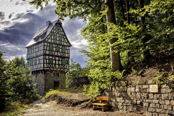 Half-timbered house in the forest, next to a paved path and a wooden bench, under sunlight with partly cloudy sky, The Herzogstuhl in the Saale Holzlandkreis district in Thuringia