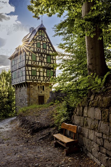 Half-timbered house in the forest, next to a wooden bench under strong sunlight, surrounded by trees and greenery, The Herzogstuhl im Saale Holzlandkreis in Thuringia