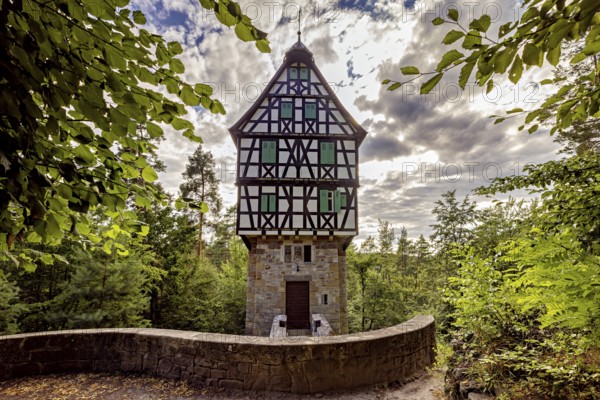 Half-timbered house in the forest surrounded by leaves, under a cloudy sky, with a curved stone wall in the foreground, The Herzogstuhl in the Saale Holzlandkreis district in Thuringia