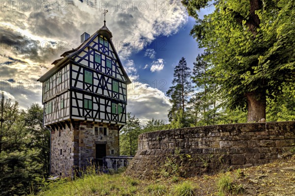 Half-timbered house on a stone base in the forest, surrounded by trees and a stone wall, under a dramatically cloudy sky, The Herzogstuhl im Saale Holzlandkreis in Thuringia